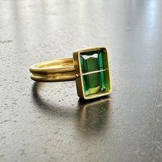 You won't be able to take your eyes off of this radiant cut green tourmaline ring. Aptly named, this stone radiates an array vibrant green hues. The double band compliments the crossbar and provides a luxurious contrast to the stone's geometric and longitudinal facets. A true one of a kind. 18k gold. 2.42 carat radiant cut green tourmaline. Size 7. Modern Green Emerald-cut Jewelry, Fine Jewelry Green Emerald Cut Emerald Ring, Fine Jewelry Green Emerald Cut Ring, Fine Jewelry Green Emerald Ring With Rectangular Stone, Fine Jewelry Green Rings With Rectangular Stone, Modern Green Emerald Cut Ring, Modern Green Ring With Rectangular Stone, Green Sapphire Open Ring Fine Jewelry, Green Tourmaline Ring For May Birthstone