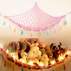 there are many stuffed animals in the hammock with string lights strung from it