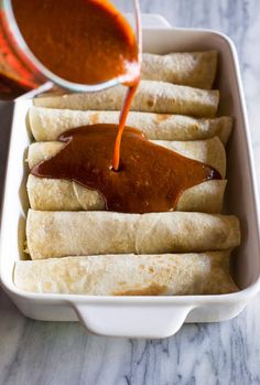 someone is pouring sauce on some food in a white dish with tortilla shells