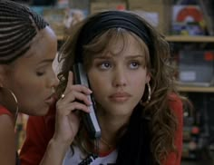 two women are talking on cell phones in a store together, one is holding her head to the other's ear