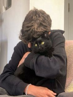 a woman sitting on top of a couch holding a black cat in her arms and looking at the camera