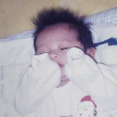 a baby laying on top of a bed covered in white blankets and covering it's eyes