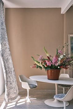 a vase with flowers sitting on top of a table next to two chairs in front of a window