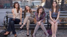 four young women sitting on a bench in front of a chain link fence and gate