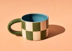 a green and white checkered coffee mug on a pink background with shadow from the cup