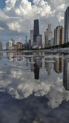 the city skyline is reflected in the still water on a sunny day with clouds and blue sky