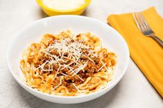 a white bowl filled with pasta and meat on top of a table next to a yellow napkin