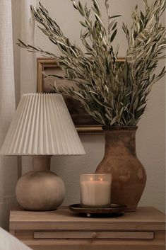 a table with a lamp, vase and candle on it in front of a mirror