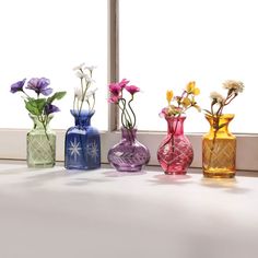 four different colored vases with flowers in them sitting on a window sill next to a window