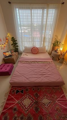 a pink bed sitting in the middle of a room next to a window with sheer curtains