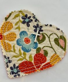 a heart shaped patch with flowers and a cross on the end is sitting in front of a white background