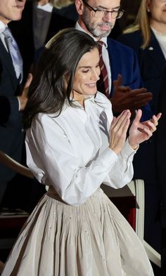 a woman in a white shirt and beige skirt clapping while standing next to other people