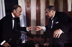 two men in tuxedos looking at each other's hands while sitting down