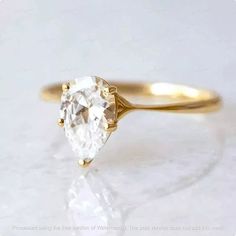 a yellow gold ring with a pear shaped diamond in the center, on a white surface