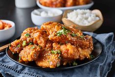 a black plate topped with fried chicken next to bowls of rice and chopsticks