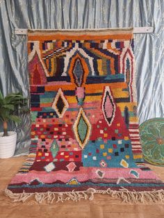 a multicolored area rug with fringes on the floor next to a potted plant