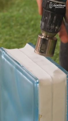 a person is using a drill to fix a piece of plastic on the ground with grass in the background