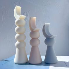 three white and gray vases sitting on top of a blue tableclothed surface