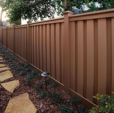 a long brown fence with stepping stones in the grass next to it and flowers growing on either side