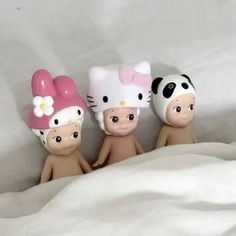 three little figurines with hello kitty hats on their heads sitting in the bed