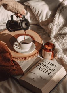 a person pouring coffee into a cup on top of a bed next to an open book