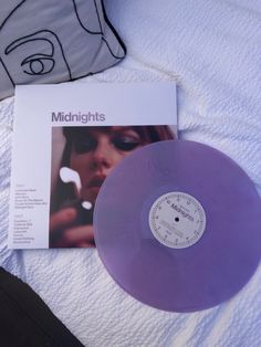 a purple vinyl record sitting on top of a bed next to a white sheet and pillow