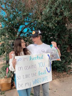 a man and woman holding a sign that says i'm hooked on asking you so take the boat to be my winto date?