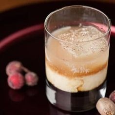 a glass filled with liquid sitting on top of a black plate next to some nuts