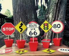 a table topped with lots of traffic signs next to a tree and potted plants