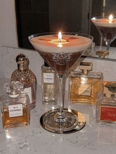 an assortment of perfumes on a counter with a candle in the middle and a martini glass next to it