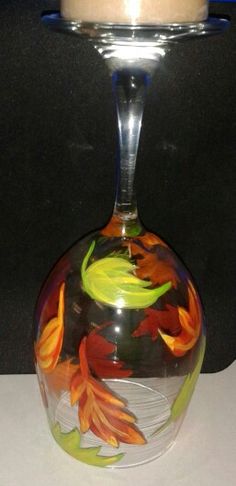 a glass vase sitting on top of a table next to a candle holder with leaves painted on it