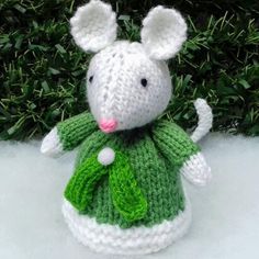 a crocheted mouse in a green dress sitting on top of snow covered ground