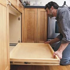 a man kneeling down in front of an open drawer on the kitchen counter top,