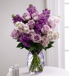 a vase filled with purple flowers sitting on top of a table next to a gift