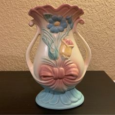 a pink and blue vase sitting on top of a wooden table next to a wall