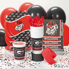 balloons, confetti and cups are on a table with black and red decorations