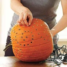 a woman is cutting into a pumpkin with wires on the table next to it and another person behind her