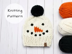 three knitted hats and two balls of yarn on a white wooden surface, one with an orange fox