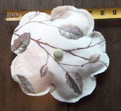 a piece of cloth with leaves on it next to a measuring tape and a button