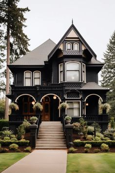 a large black house with lots of windows and plants on the front lawn, along with steps leading up to it