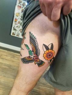 a man with a tattoo on his leg holding a flower and two birds in flight