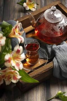 a glass tea pot and cup on a wooden tray with flowers