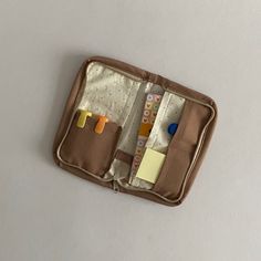 an open brown case filled with lots of different types of pens and paper on top of a white surface