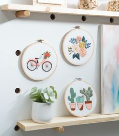 three cross stitch hoops hanging on a wall next to a potted plant and two paintings