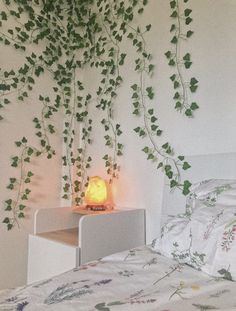 a bed with white sheets and green vines on the wall above it, next to a night stand