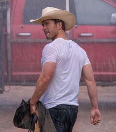 a man walking in the rain with a cowboy hat on his head and holding a bag