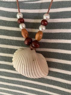 a necklace with shells and pearls on a striped fabric background is seen in this image