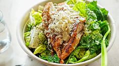 a white bowl filled with salad and meat on top of a table next to a glass of water