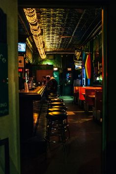 a dimly lit bar with several stools in the foreground and lights on the ceiling