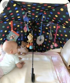 a baby laying on top of a bed next to an umbrella with toys hanging from it